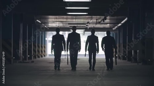 Black silhouettes of four men walking towards the camera in the car parking photo