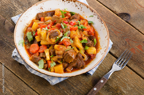 Beef stew with vegetables on a wooden table.