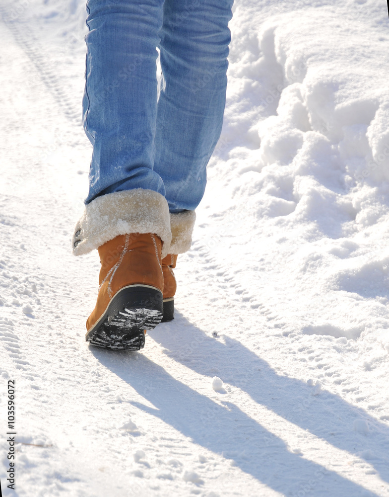 Girl in jeans and yellow boots goes on snow-covered road
