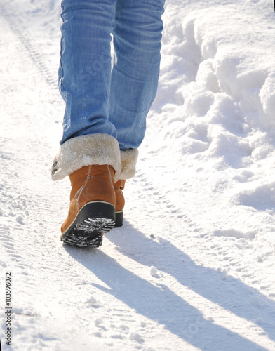 Girl in jeans and yellow boots goes on snow-covered road