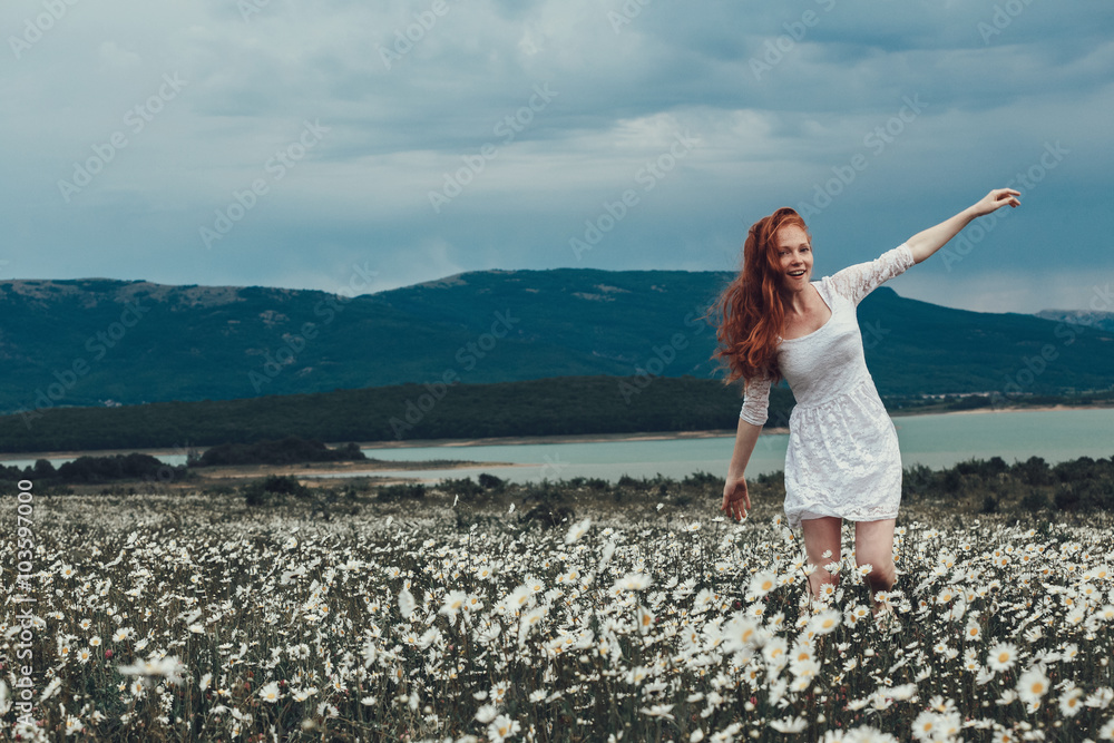 Beautiful young girl with curly red hair in chamomile field