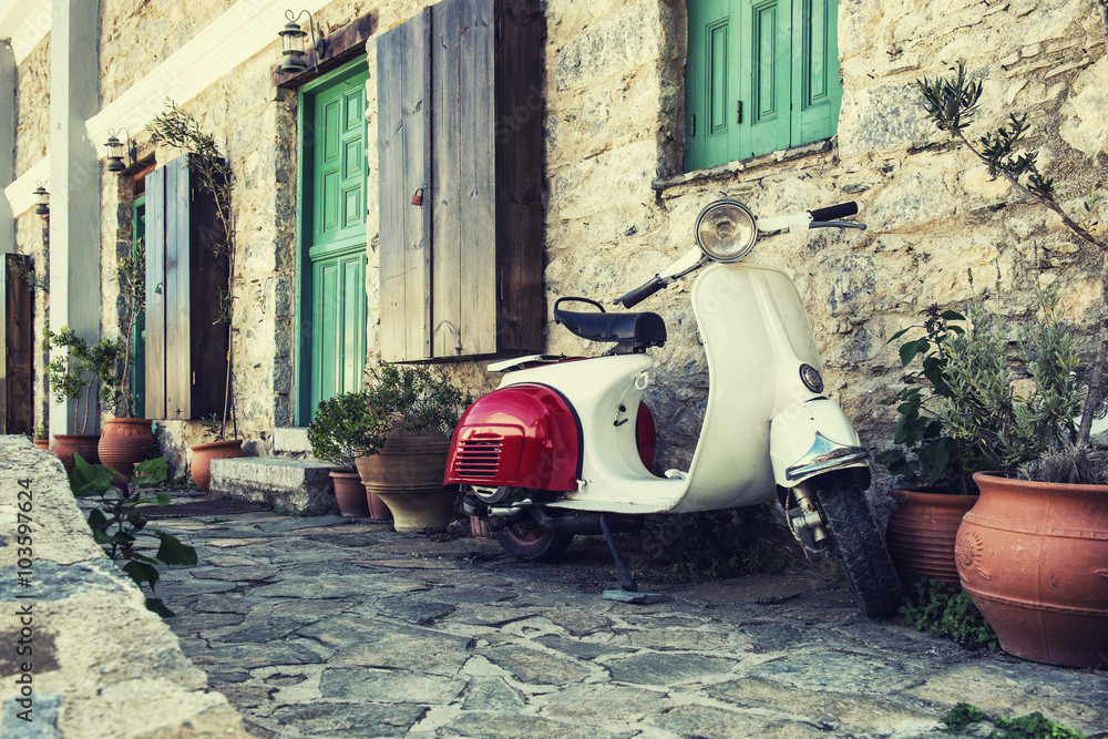 Naklejka premium Stary skuter zaparkowany pod ścianą przy pustej ulicy Karpathos w Grecji. Post przetworzony z filtrem vintage.