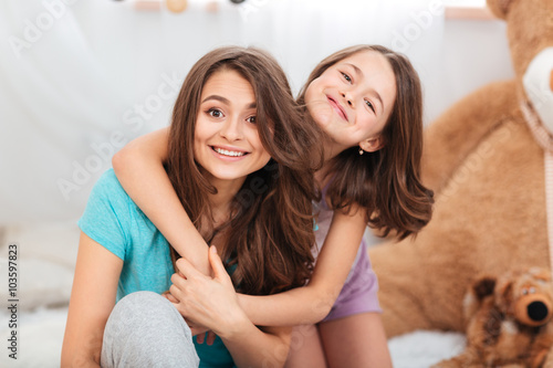 Two happy lovely sisters sitting and hugging at home photo