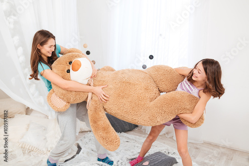 Two cheerul playful sisters playing with big plush bear photo