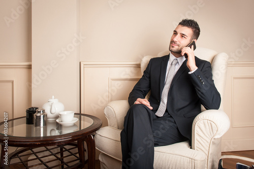 Young businessman talking at mobile phone sit on armchair.