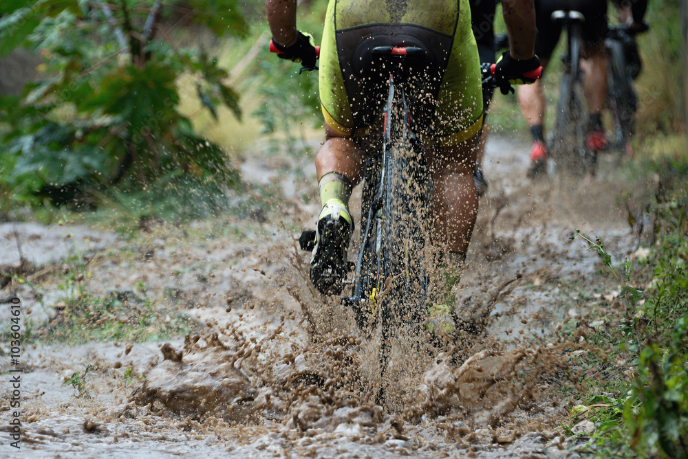 Fototapeta premium Mountain bikers driving in rain upstream creek
