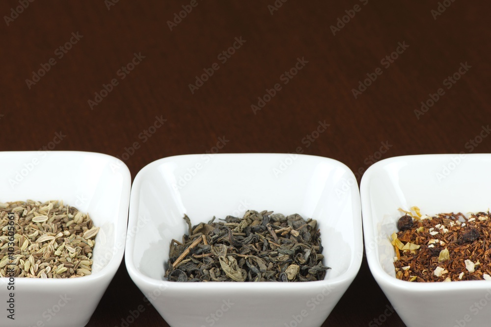 Three sorts of tea leaves in square plates on brown wooden table, positioned horizontally with space for text above Three sorts of tea leaves in square plates on brown wooden table, positioned horizontally with space for text above