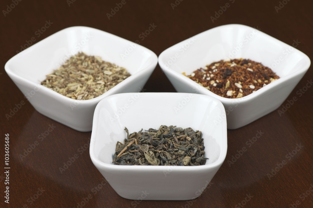 Three sorts of dry tea leaves in square plates on brown wooden table with reflection Three sorts of dry tea leaves in square plates on brown wooden table with reflection