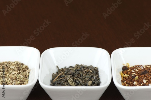 Three sorts of tea leaves in square plates on brown wooden table, positioned horizontally with space for text above