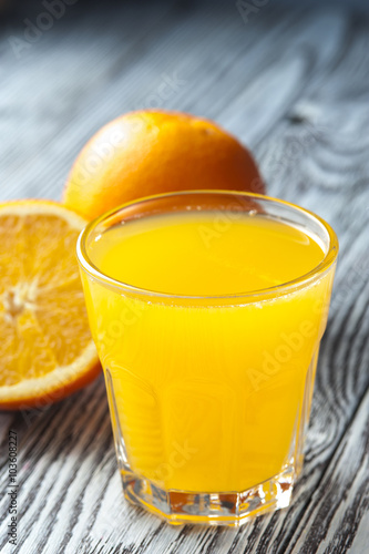 Glass of fresh orange juice and ripe oranges on wooden table. Focus on glass.