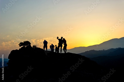 Silhouettes of people resting on top of rock and looking at golden sunset