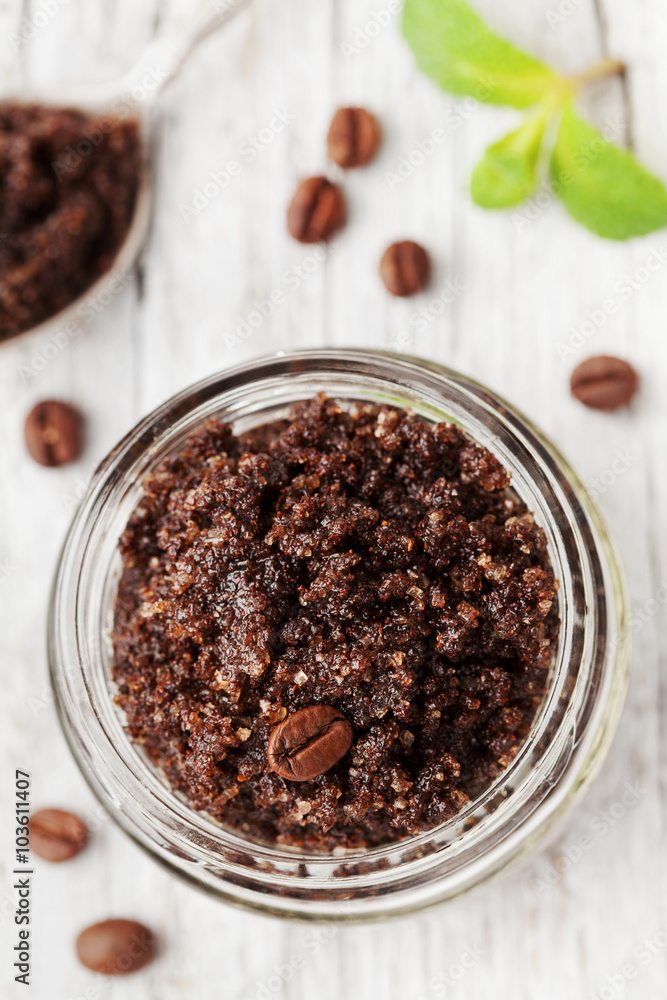 Body scrub of ground coffee, sugar and coconut oil in glass jar on white rustic table, homemade cosmetic for peeling and spa care, top view Body scrub of ground coffee, sugar and coconut oil in glass jar on white rustic table, homemade cosmetic for peeling and spa care, top view