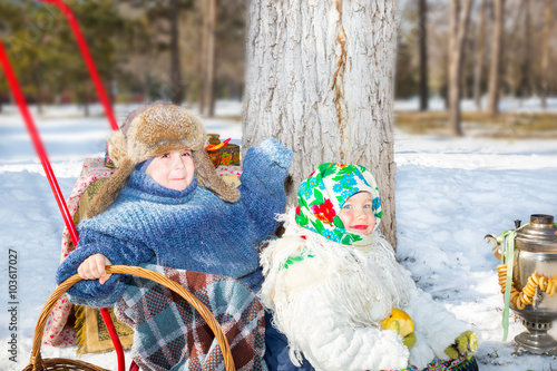 Children in Russian pavloposadskie scarf on head with floral print on snow.  Russian style on a background of samovar and with  bagels photo