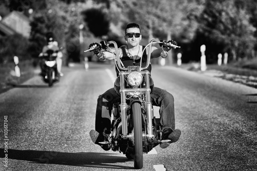 Tough, tattooed biker with his chopper in motion on the road