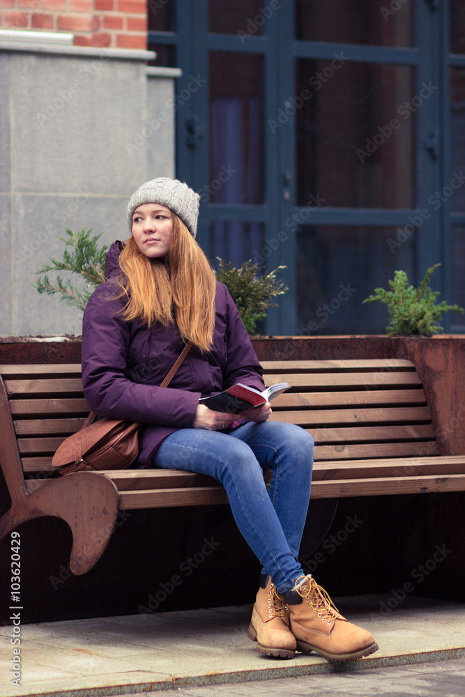 Teen red haired girl sitting and reading a book outdoors Teen red haired girl sitting and reading a book outdoors