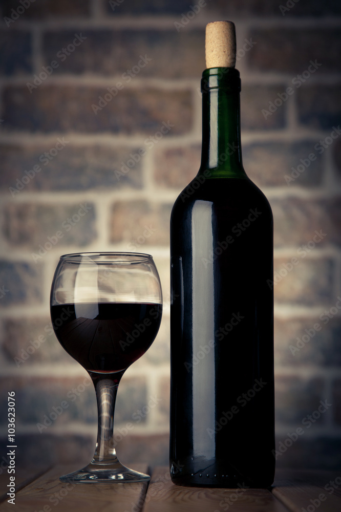 Wine bottle and glass on a wooden table with bricks wall backgro