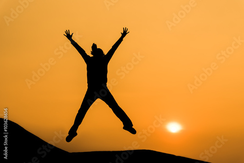 Silhouette of woman in happy jump on orange sunset sky