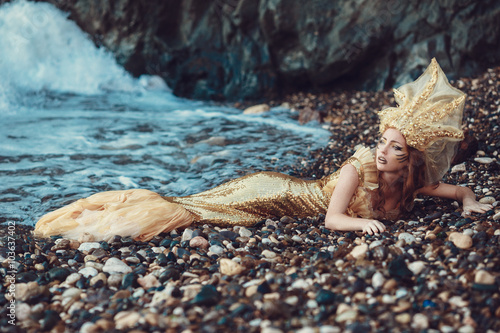 Beautiful fashionable mermaid sitting on a rock by the sea photo