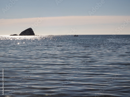 Roca negra como un islote en el horizonte del mar azul en verano, España.