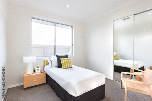Modern bedroom with a single bed and white sheets near a mirror