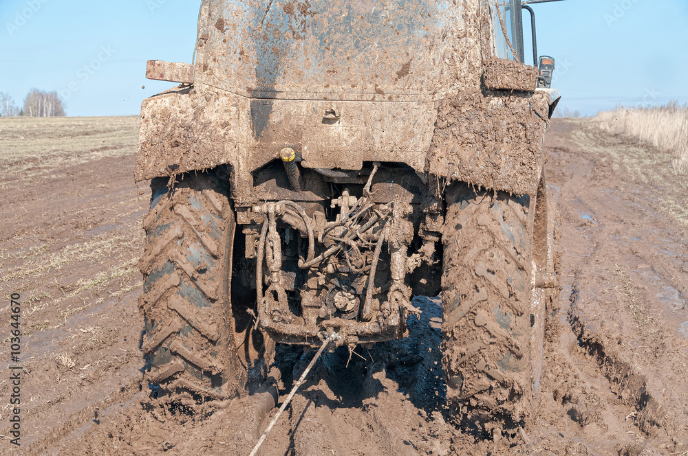 Obraz premium Wheeled tractor tows in mud on dirty road in fallow field 