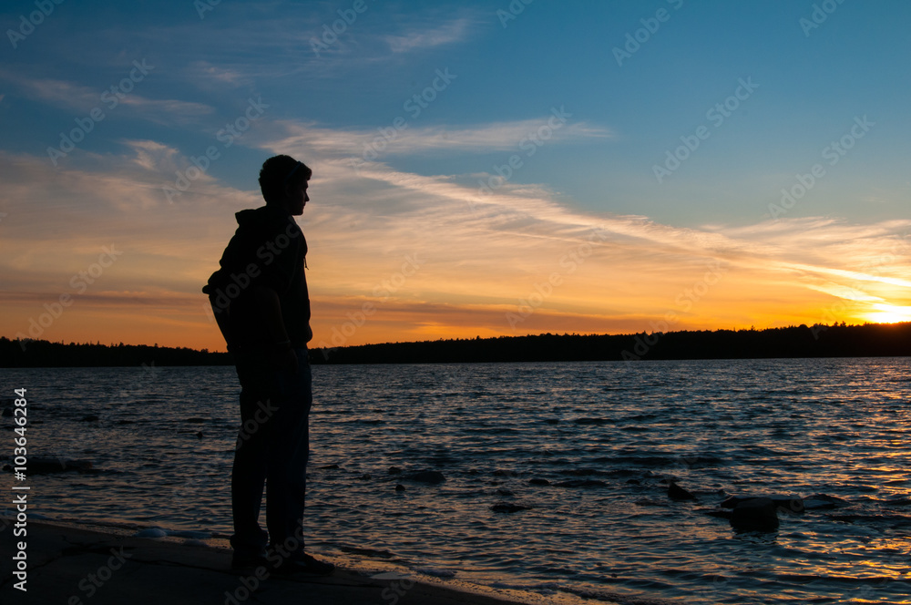 teenage boy watches the sun rise over a lake
