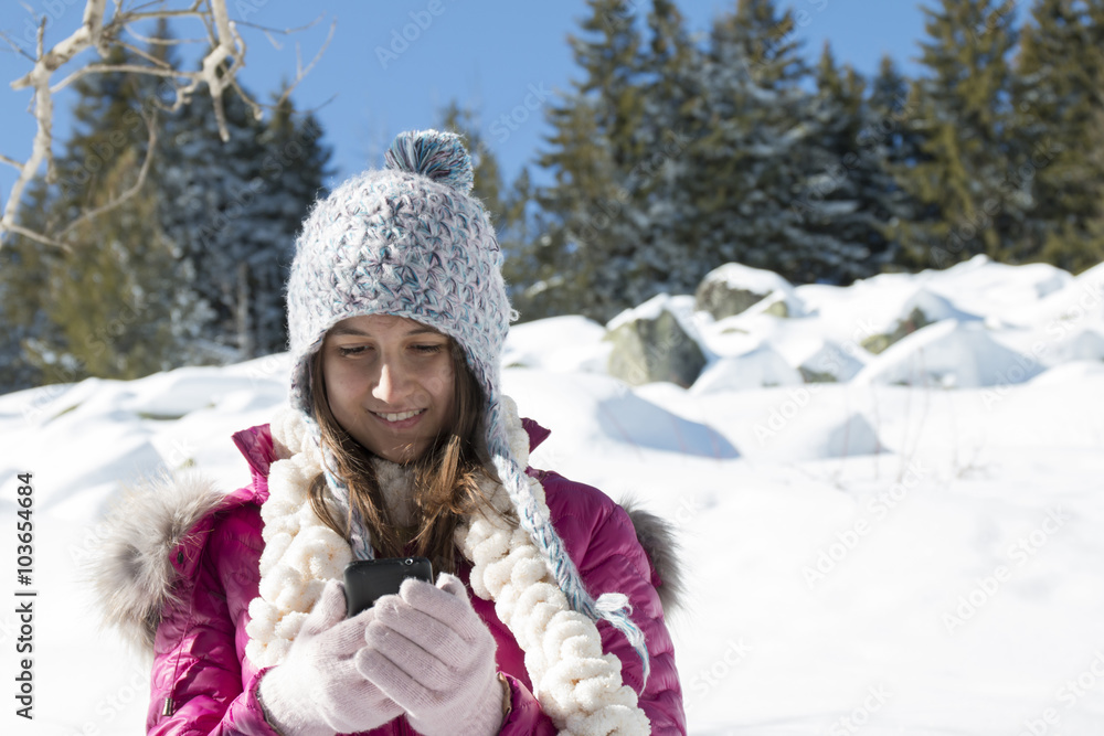 Fototapeta premium A young girl with a smartphone in the mountains in winter
