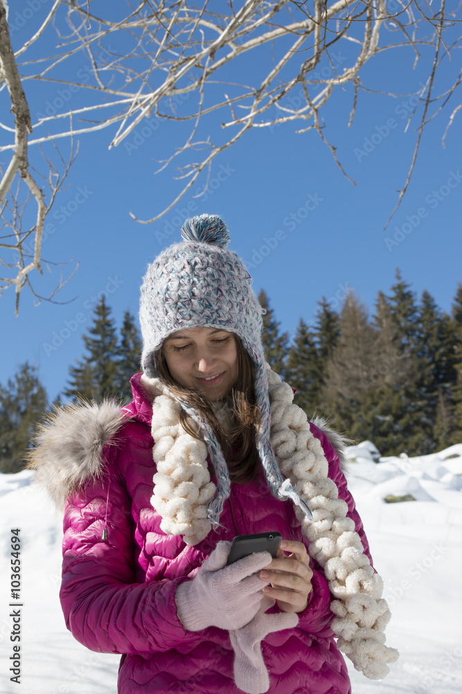 Fototapeta premium A young girl with a smartphone in the mountains in winter