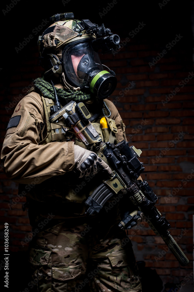 Soldier with rifle and respirator on dark background/Man in military uniform with mask, helmet and rifle on dark wall background looking at camera
