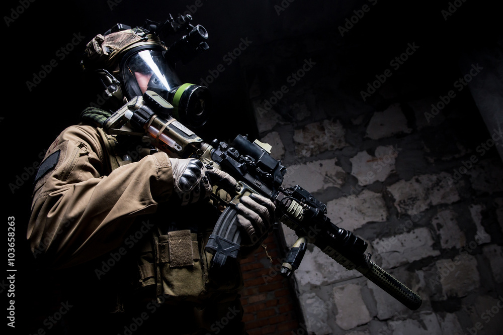 Low angle shot of soldier in respirator with weapon/
Man in uniform with helmet and mask on his face holding rifle and looking away