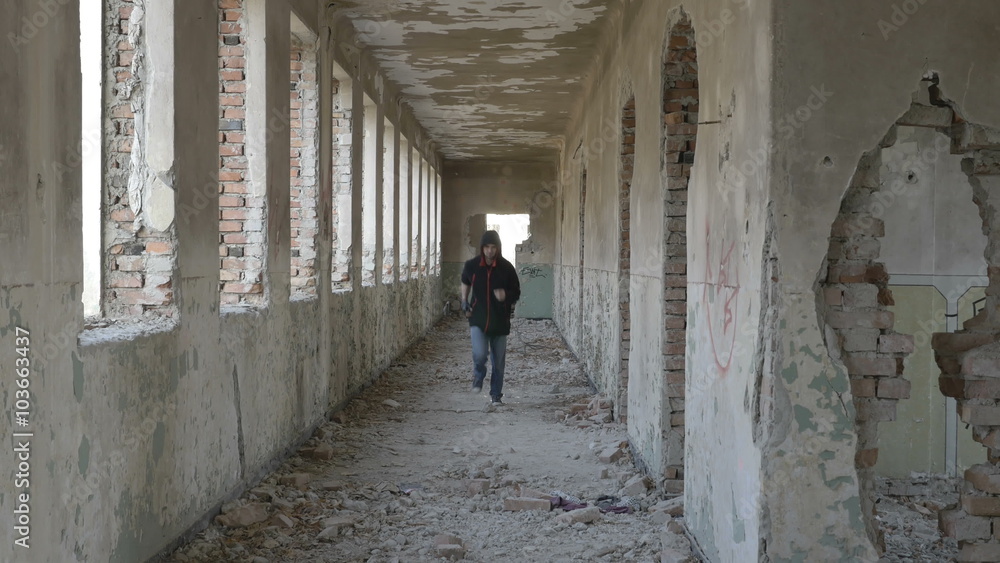 Hooded frightened young man running in an abandoned military building Hooded frightened young man running in an abandoned military building