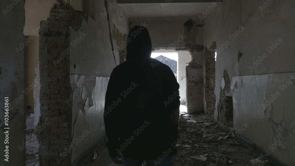 Hooded young man walking through the hallway of an abandoned building Hooded young man walking through the hallway of an abandoned building