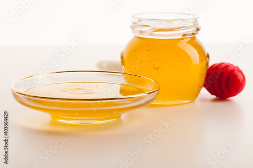 Sweet sticky golden fluid on transparent plate next to glass jar