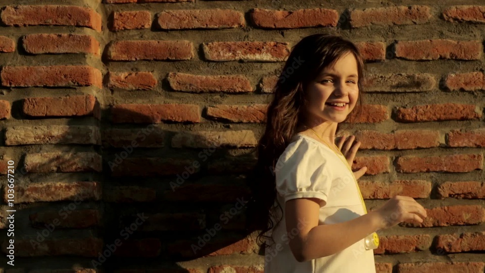 beautiful little girl near brick wall looking at the camera and playing with her hair beautiful little girl near brick wall looking at the camera and playing with her hair
