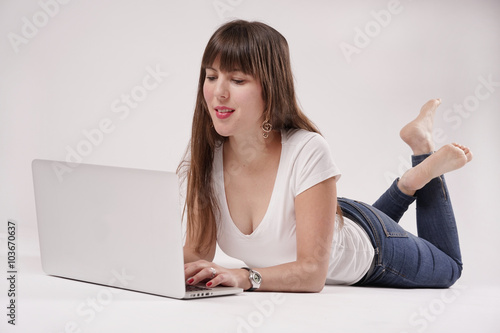 Eine junge Frau, Mädchen liegt barfuß auf dem Boden, vor ihr steht ein Laptop