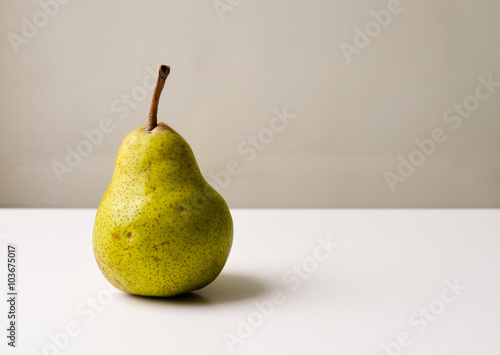 Green and brown pear on a white table against a neutral background