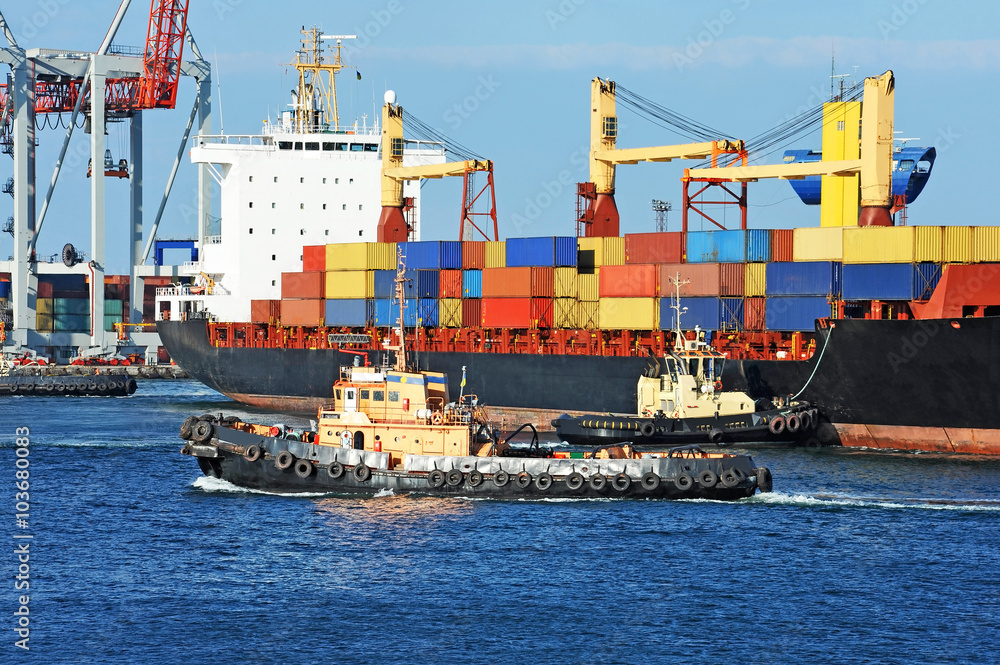 Fototapeta premium Tugboat assisting container cargo ship to harbor quayside