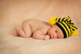 новорожденный лежит на животе в полосатой шапке пчелке
