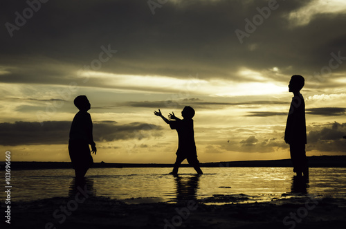 silhouette image concept of young boys playing at the beach with beautiful sunrise sunset background. sandy beaches and reflection on water