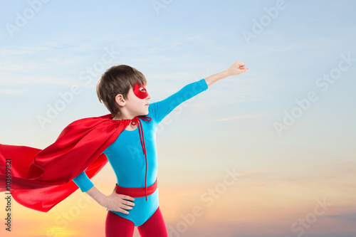 Superhero kid flying on sunset sky.