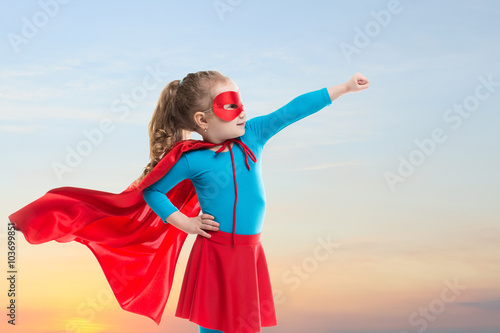 Little child girl plays superhero. Child on the background of sunset sky.