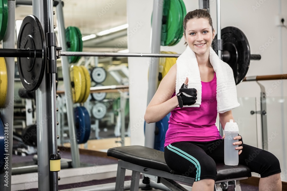 Smiling woman sitting on barbell bench and showing thumb up Smiling woman sitting on barbell bench and showing thumb up