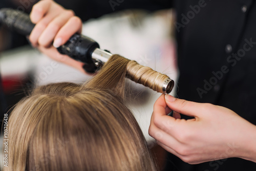 curling woman's hair giving a new hairstyle at hair salon close-up
