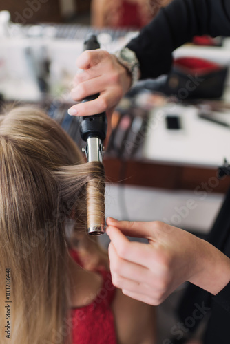 curling woman's hair giving a new hairstyle at hair salon close-up