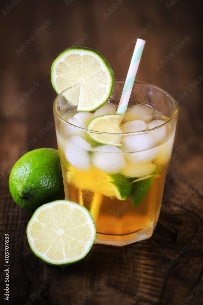 Cold tea with ice cubes and lime on dark rustic wooden background Cold tea with ice cubes and lime on dark rustic wooden background