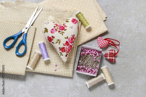 Sewing set: fabrics, threads and pins on pink background