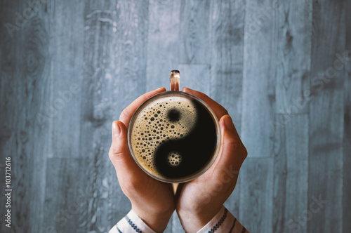 Fotografie Girl holding a coffee cup with ying and yang symbol.