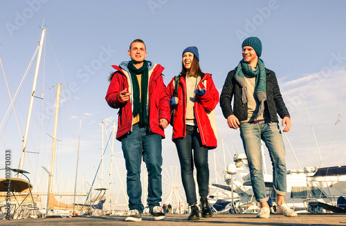 Young friends walking at pier - Cheerful teenagers on vacation smiling at harbor ferry wheel  park in a sunny winter day - Concept of friendship and happiness with cheerful people on holiday © akhenatonimages