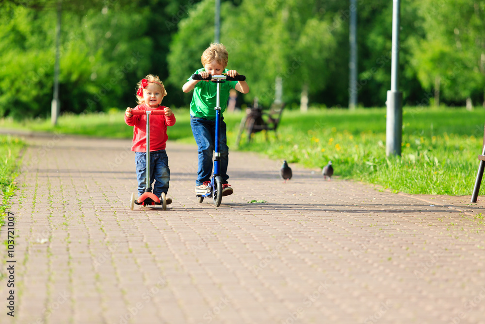 little boy and toddler girl riding scooters in summer