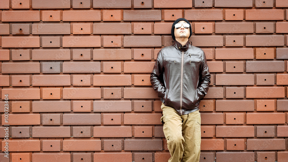 An Asian Man in a Brown Jacket Leans Against the Wall